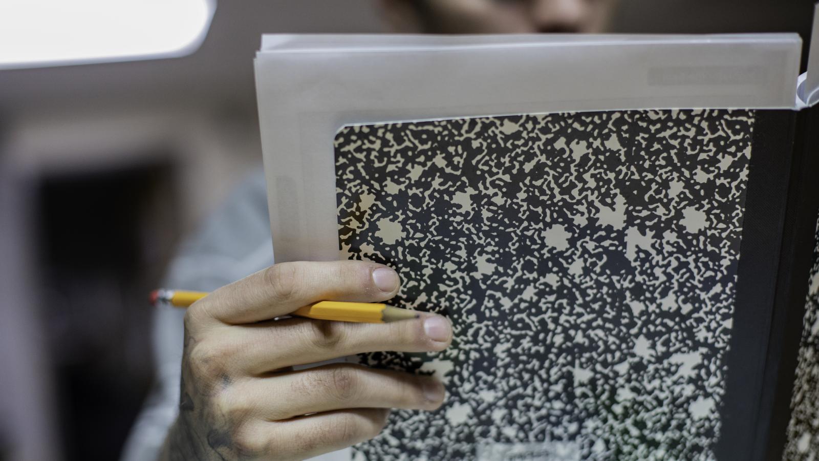 Close-up view of teenage student holding a composition book and pencil