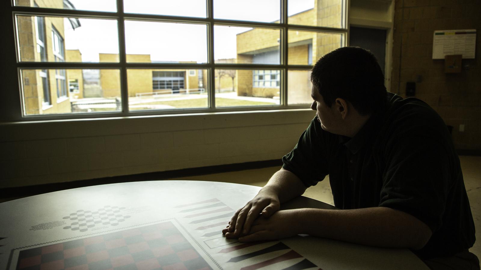 Teenage student sitting alone at table, looking out a window