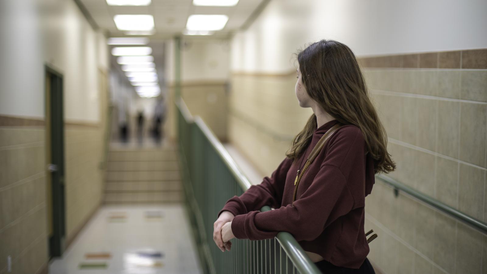 Teenage student standing in empty school hallway