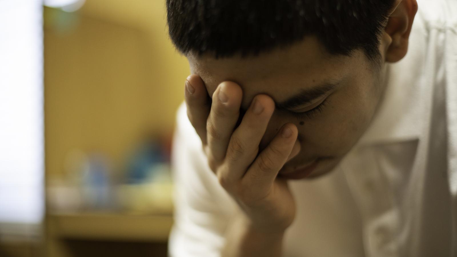 Close-up of teenager sitting, holding their face in their hands