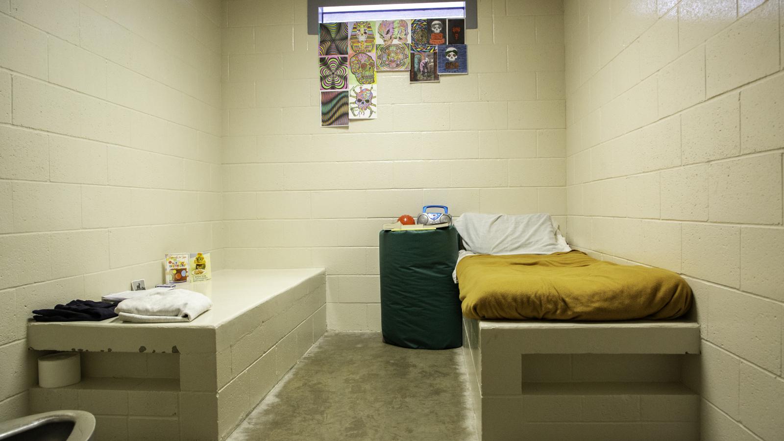 Interior view of a juvenile detention facility room with a bed and small window