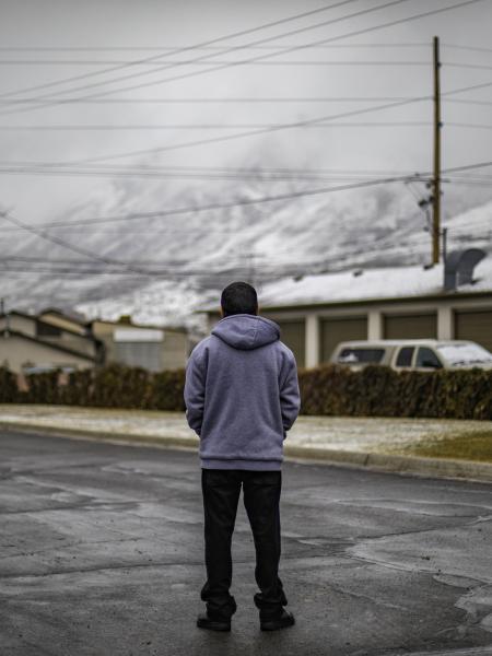 Teenager with back to camera, standing on a deserted street facing a distant, snow-capped mountain range